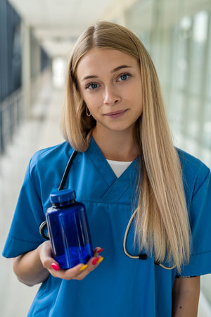 beautiful young nurse in uniform holding a blue bottle with medicine in her hands in the hospital....