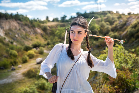 Native American female holding bow and arrow posing at nature. lifestyleの写真素材