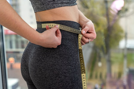 beautiful young woman takes measurements with a tape of her body after a workout in the gym. sport...