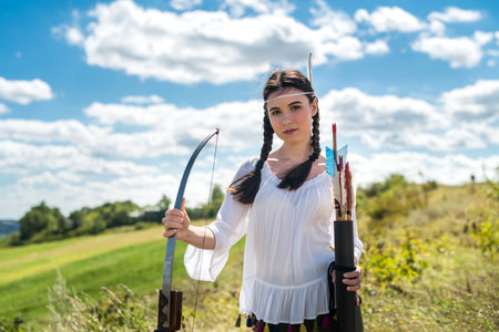 Native American female holding bow and arrow posing at nature. lifestyleの写真素材