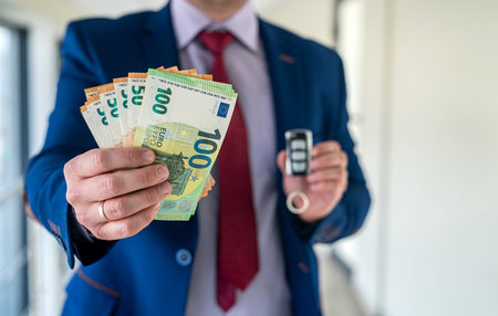 a man in a suit holds euros and car keys. rent or purchase auto. shopping conceptの写真素材