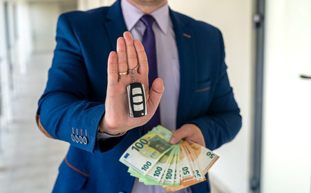 a man in a suit holds euros and car keys. rent or purchase auto. shopping conceptの写真素材