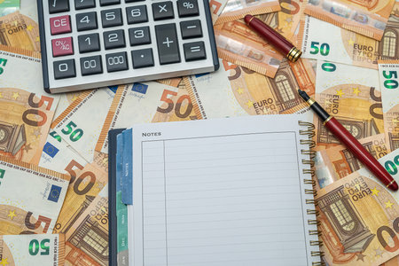 new beautiful red pen calculator with open balcony lying on scattered new euro bills. money conceptの写真素材