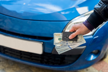 male hands in a business suit holding dollars and car keys on a background of blue beautiful car. business concept. The concept of buying a car. business conceptの写真素材