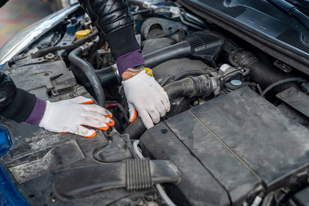 a professional mechanic in special clothes and gloves repairs a car with an open hood at a car service. car repair concept.の写真素材