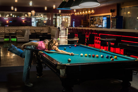 cheerful young woman playing billiard in pub. relax after hard day