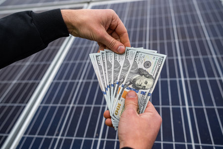 boss in a jacket with young hands holding a large sum of dollars on a background of solar panels....