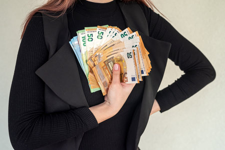 Beautiful young girl in a stylish black suit holds a large sum of new euros in his hands. big business conceptの写真素材