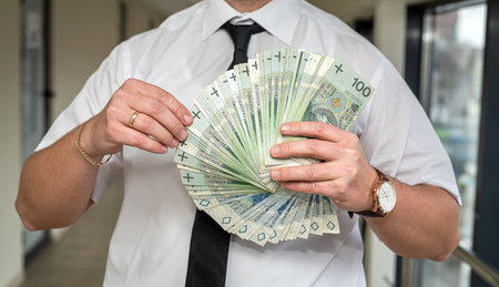 Handsome businessman who earns a lot holds zlotys in his hands to invest money. Earning concept