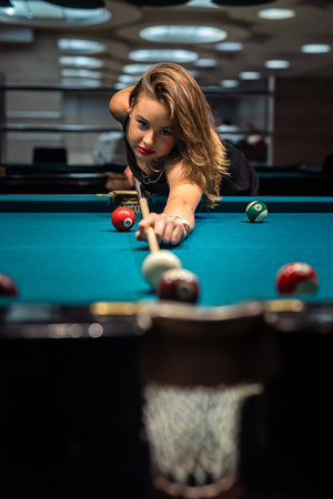 Young happy girl holding cue and play billiard at pub. lifestyle