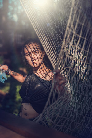 portrait of young woman wear short shorts with knife in forest.Woman smeared in the swamp holding a dagger posing in the woodsの写真素材