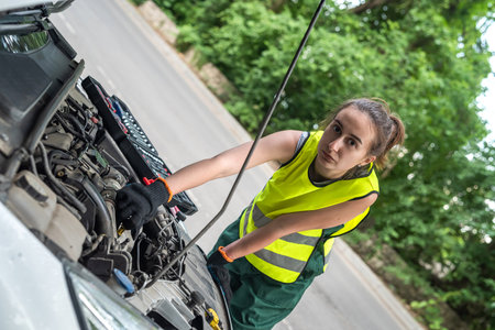 portrait of a young female mechanic in uniform near a broken car, outdoorの写真素材