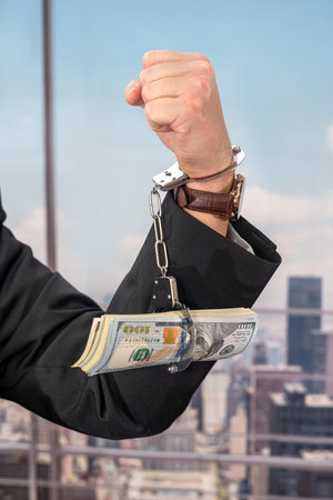 young male businessman in a classic suit and tie holds his hands in handcuffs. The concept of a man in handcuffsの写真素材