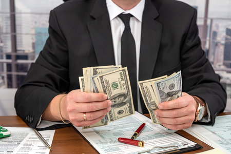 young stylish businessman counts a large sum of dollars and fills out tax forms 1040 in his office. The concept of big business and profits from itの写真素材