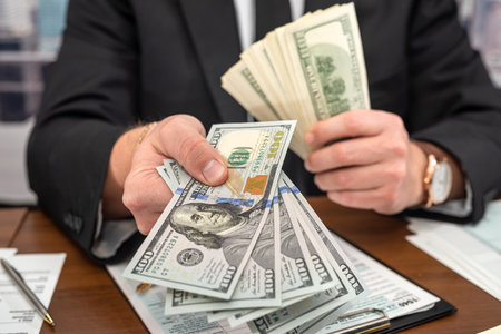 young businessman in a black stylish suit at a spacious table counts dollars and fills out forms. The concept of tax forms and dollarsの写真素材