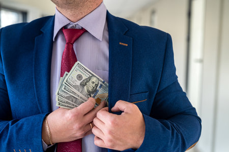 Man in blue suit and red tie putting bribe dollar bills into his pocket. corruption conceptの写真素材