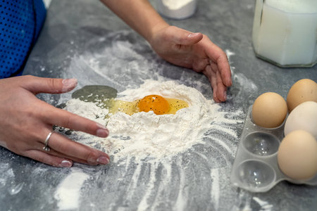 young beautiful woman is fighting in the kitchen breaking eggs into flour and kneading dough into dumplings. The concept of cooking in the kitchenの写真素材