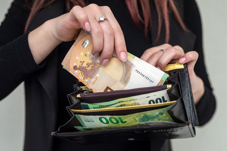 Beautiful young girl in black wants to pay euros from a wallet in a clothing store. business concept