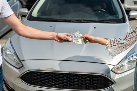 female hand gives dollar to a salesman when buying a new modern car, sale conceptの写真素材