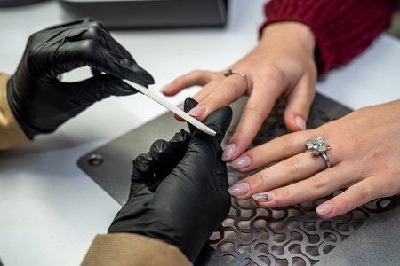 the manicurist in special gloves holds the client's hand and works with it during the epidemic. manicure concept. Cosmetology conceptの写真素材