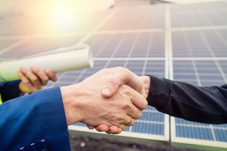 workers in overalls and helmets two men shake hands after working on the installation of panels. The concept of green electricity to maintain the environmentの写真素材