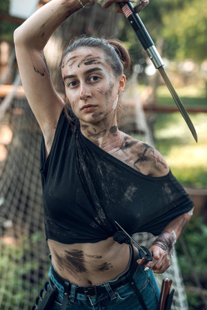 beautiful young girl in dirty ragged clothes with swords and knives in the woods trains. Concept of an armed girl in the woodsの写真素材