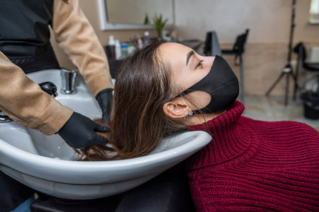 in the new prestigious salon, a master in special gloves prepares a client to wash her head in a special chair during an epidemic. hairdressing concept. beauty salon conceptの写真素材
