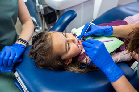 little girl sitting in a dental chair and two female dentists treating baby teeth. Two female dentists entertain a little patientの写真素材