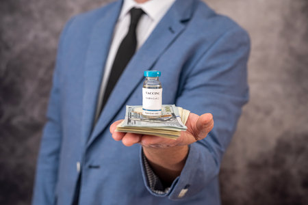 handsome handsome man in a chic suit from a cool brand holds a vaccine and dollars. Vaccination concept during a pandemic in isolationの写真素材