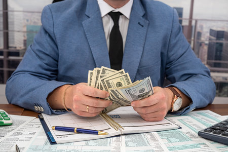 strict angry businessman in a suit from a stylist makes calculations on his own business at the table in the office. The concept of tax forms and businessの写真素材