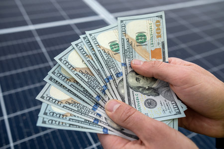 hand of a young man holding dollars for the installation of new solar panels. green electricity conceptの写真素材