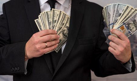 Young man in suit putting dollar bills in his pocket. Concept of bribery or corruption