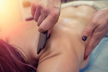 Young beautiful woman receiving hot stone massage and relaxing in spa. Black stones on the back of a lying womanの写真素材