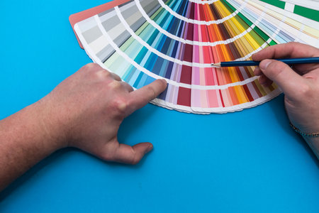 male hand choosing paint tone at color sampler isolated on blue background. different colorsの写真素材