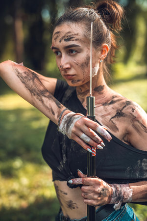 beautiful young girl in dirty ragged clothes with swords and knives in the woods trains. Concept of an armed girl in the woodsの写真素材