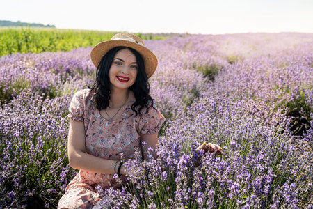 young brunette in a straw hat sits on a background of lavender in a white polka dot dressの写真素材