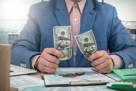businessman counts dollars by filling out US tax forms 1040, concept of cost and profit calculationの写真素材