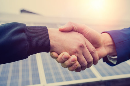 two young handsome men in overalls and caste shake hands after installing power panels. green electricity conceptの写真素材