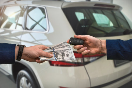 the seller of a luxury car dealership gives the owner the car keys and the other pays for the dollars. The concept of buying a carの写真素材