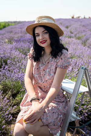young brunette in a straw hat sits on a background of lavender in a white polka dot dressの写真素材
