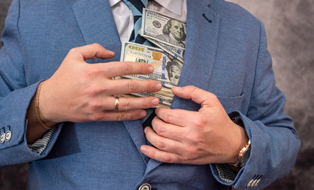 a man with a strong physique in a shirt and jacket holds his own earned dollar bills. The concept of a good big profit in dollarsの写真素材