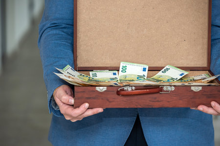 young boss businessman in expensive suit with tie holds suitcase with euro banknotes. The concept of the euro in a suitcase for a man with the taxの写真素材