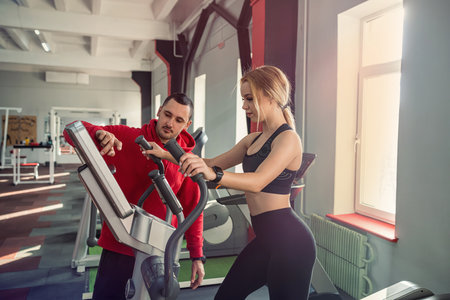 Fit female client running on treadmill with her personal trainer in a sport centre. sports lifestyle
