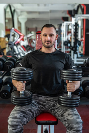 Handsome young man with a beautiful figure works as a fitness trainer in a prestigious gym. Husband...