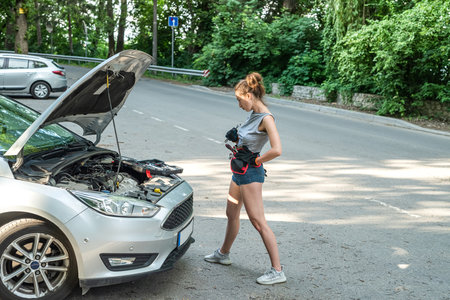 Beautiful young woman open hood and fixing the car on the roadside. broken-down auto