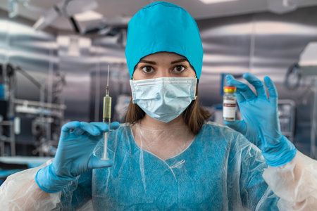 Portrait of a female doctor in a face mask wearing gloves prepares a syringe with medicine in the operating room. healthcare concept. preparation for surgery. patient's healthの写真素材