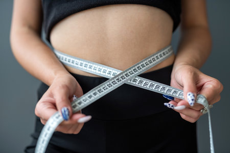 Close-up of a standing fitness woman measuring her waist with a tape with numbers. waist of a woman with a beautiful relief. Healthy Lifestyleの写真素材