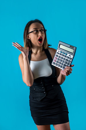 Beautiful young business woman in glasses holding a calculator isolated on a blue background. Career achievement wealth .business accounting concept.の写真素材