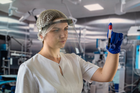 young nurse doctor in protective uniform glove and mask looks at blood samples in operating room...