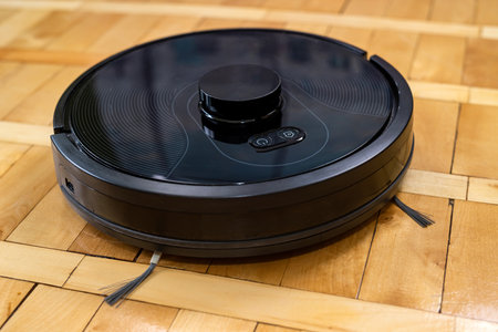 robot vacuum cleaner on a laminated wooden floor with a remote control. smart cleaning technology. robotの写真素材